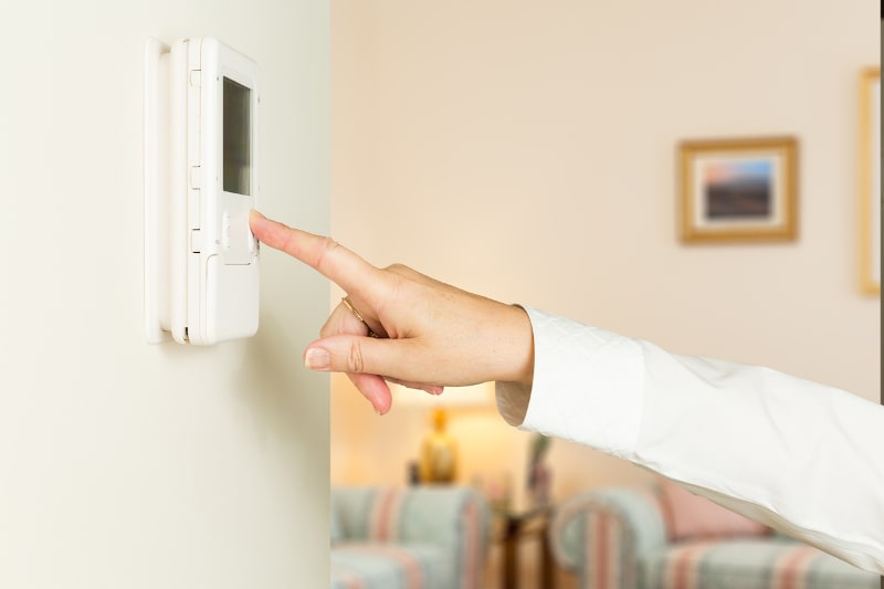 hand reaching out to adjust thermostat on cream colored wall